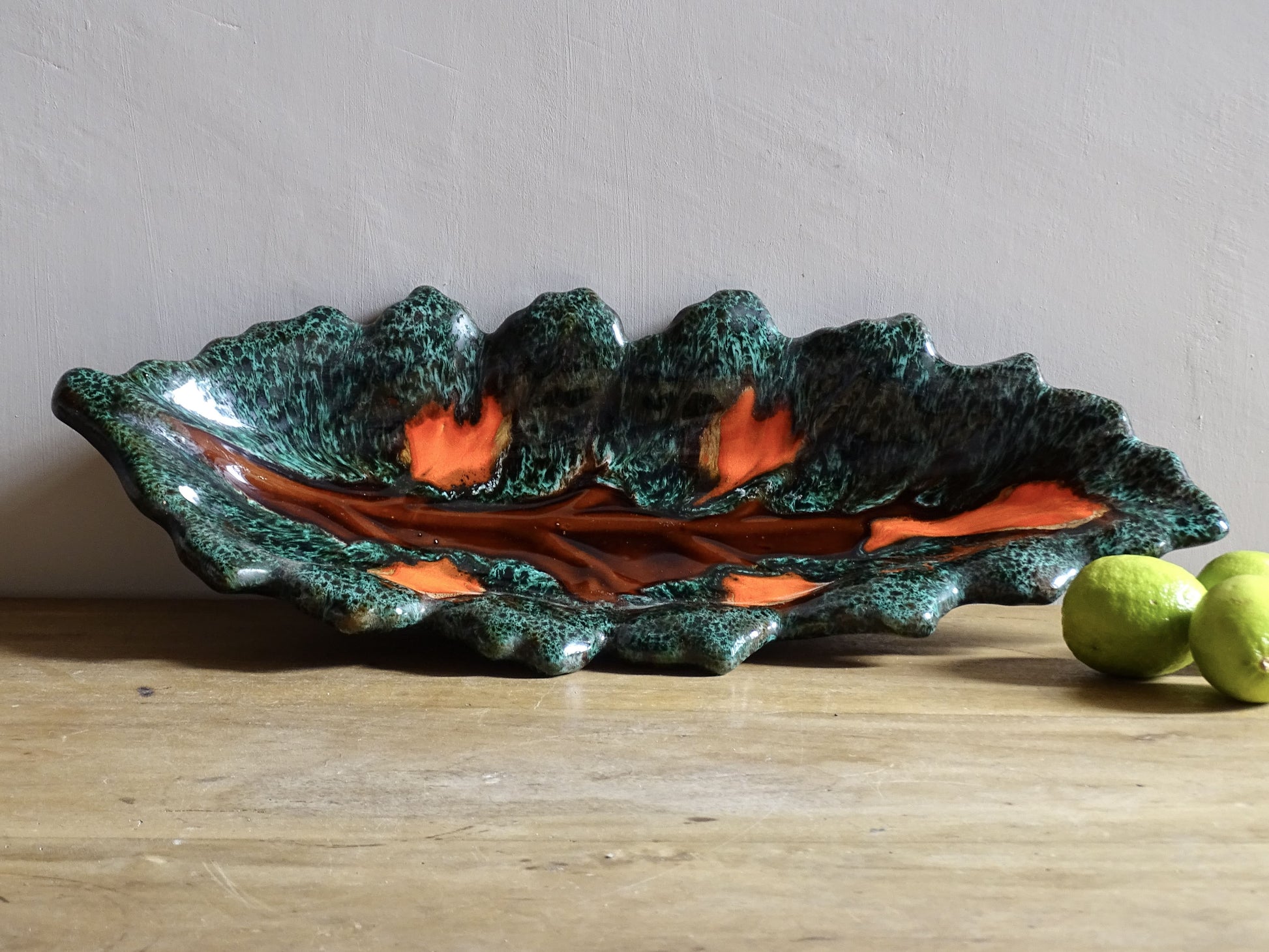 Large French vintage Vallauris ceramic bowl in the shape of a leaf. It is glazed with a dark green with details in brown and orange.