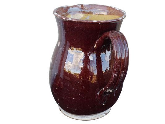 Brown French antique pottery pitcher with yellow glaze interior. Timeworn ceramic jug with handle and spout.