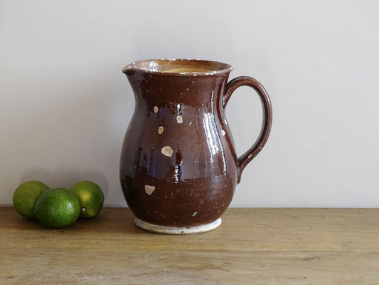 Brown French antique pottery pitcher with yellow glaze interior. Timeworn ceramic jug with handle and spout.
