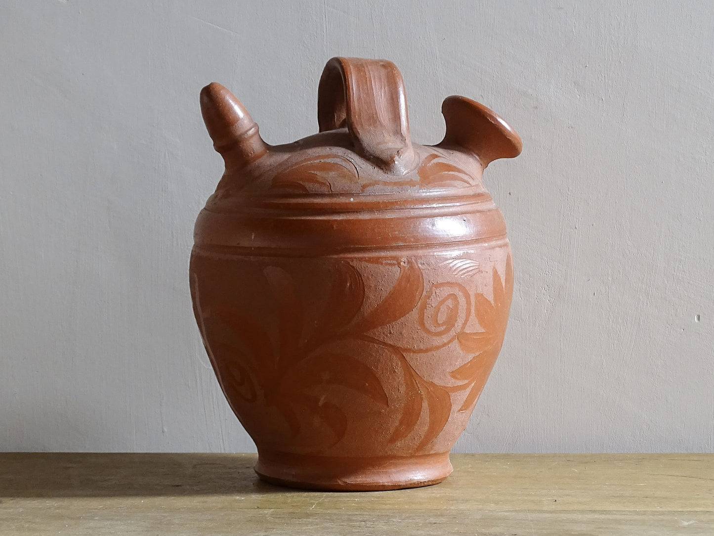 French vintage ceramic gargoulette in a deep red colour with floral detailing. The body of this terracotta jug is a rounded shape with a handle to the top and two spouts.