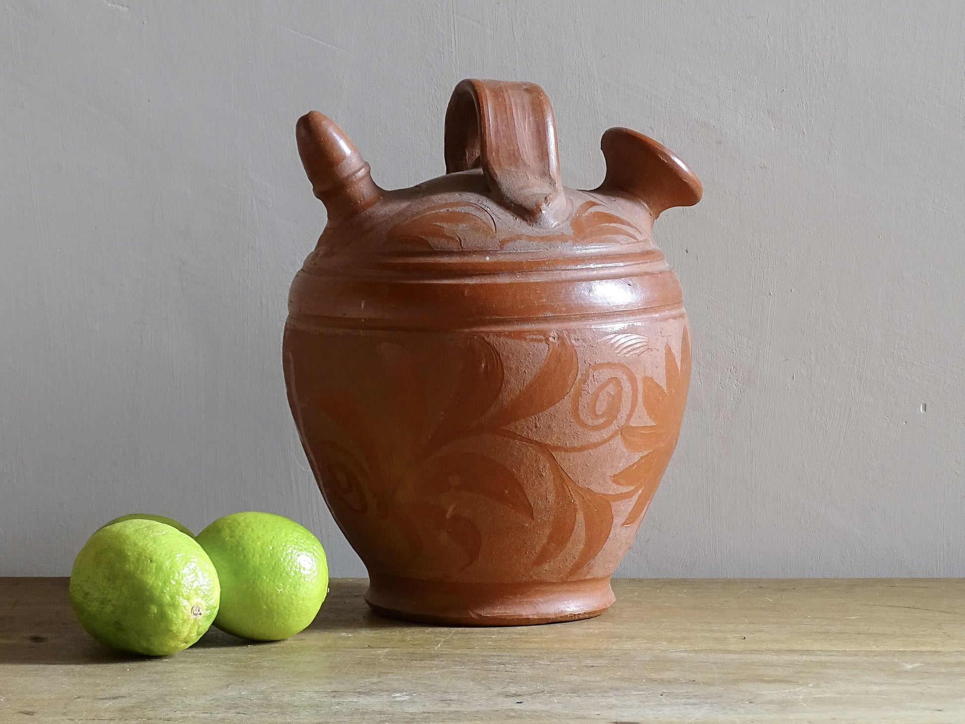 French vintage ceramic gargoulette in a deep red colour with floral detailing. The body of this terracotta jug is a rounded shape with a handle to the top and two spouts.