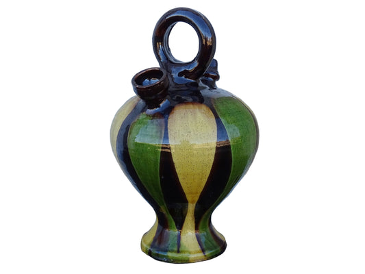 French antique pitcher or gargoulette. Terracotta jug with a green and yellow striped glaze on a dark brown background. It has a curved shape with a round handle to the top and two spouts.
