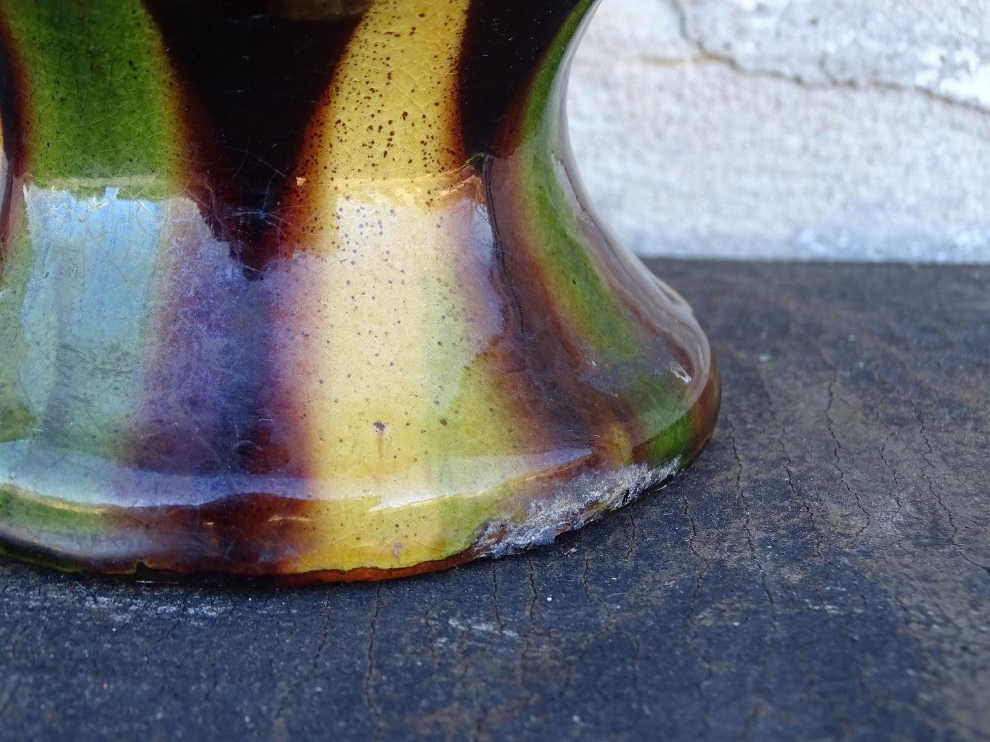 French antique pitcher or gargoulette. Terracotta jug with a green and yellow striped glaze on a dark brown background. It has a curved shape with a round handle to the top and two spouts.
