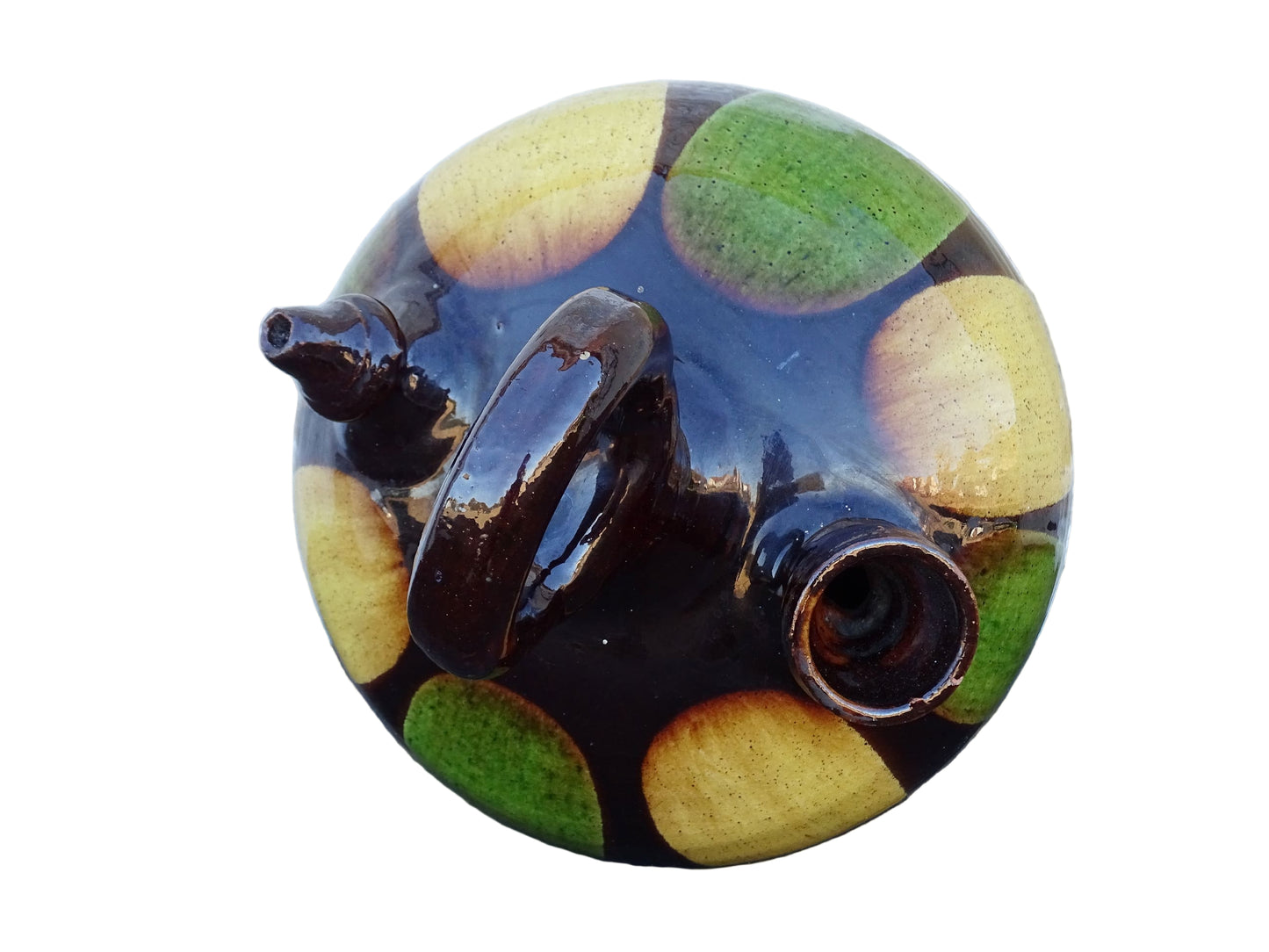 French antique pitcher or gargoulette. Terracotta jug with a green and yellow striped glaze on a dark brown background. It has a curved shape with a round handle to the top and two spouts.