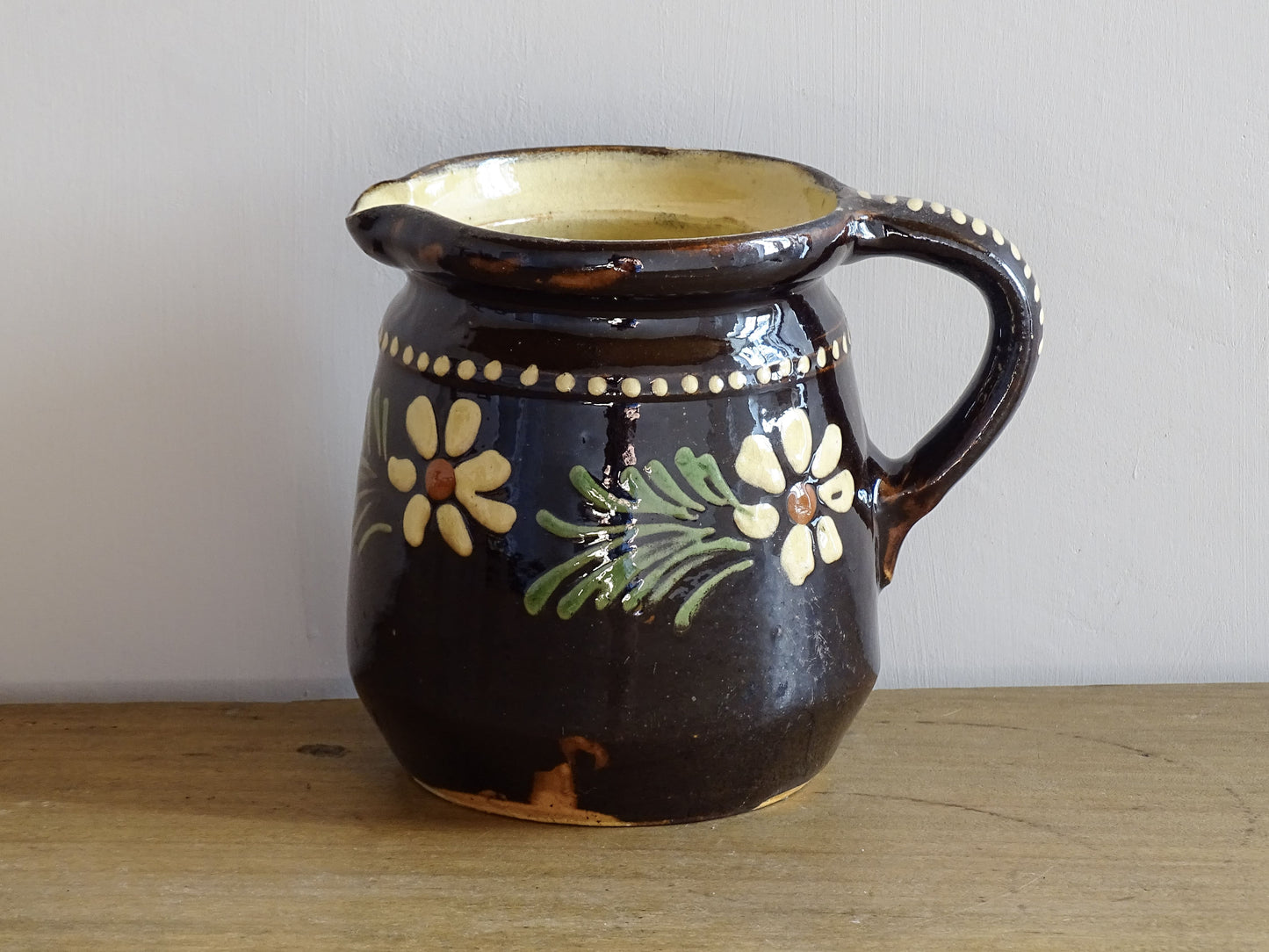French vintage ceramic pitcher from Alsace. Pottery jug with brown glaze and hand painted with flowers, leaves and dots.