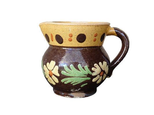 Small French vintage pottery pitcher from Alsace. Ceramic jug with a brown glaze and yellow glazed stripe around the top. It is hand painted with white flowers, green leaves and dots.
