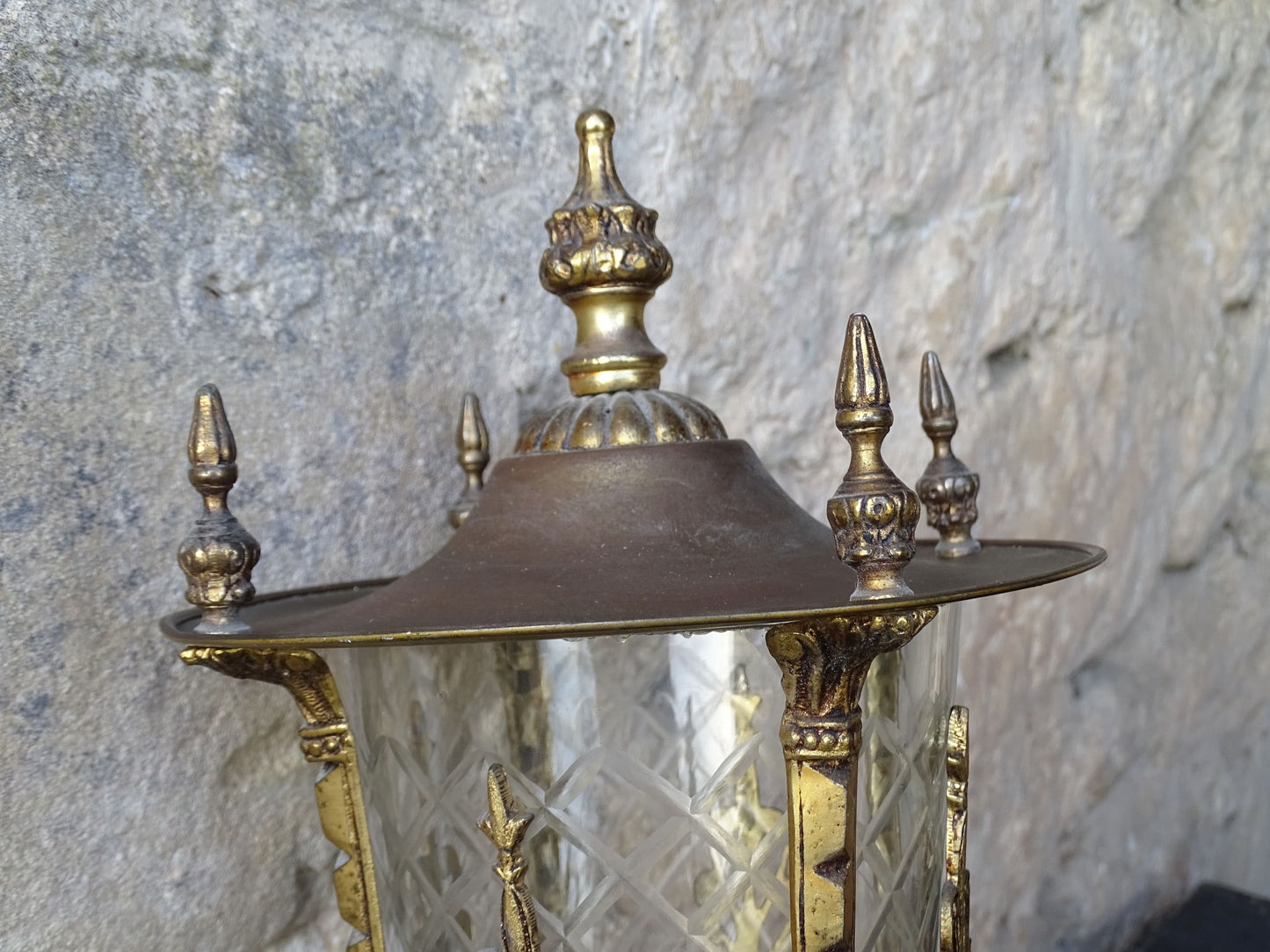 A beautiful French vintage wall light made from gilded metal with a clear cut-glass lantern. The frame has small finials to the top, leaf motifs around the sides, and an ornate scrolling arm. The glass has a diamond pattern.