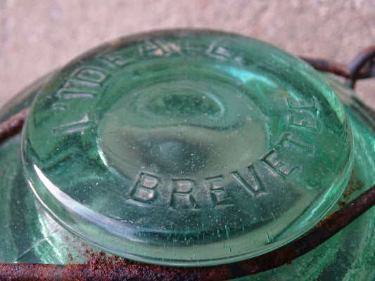 Pair of French vintage green glass preserving jars by L'Ideale. They have thick glass, embossed with the maker's name on top and original metal fasteners with a naturally aged finish. 