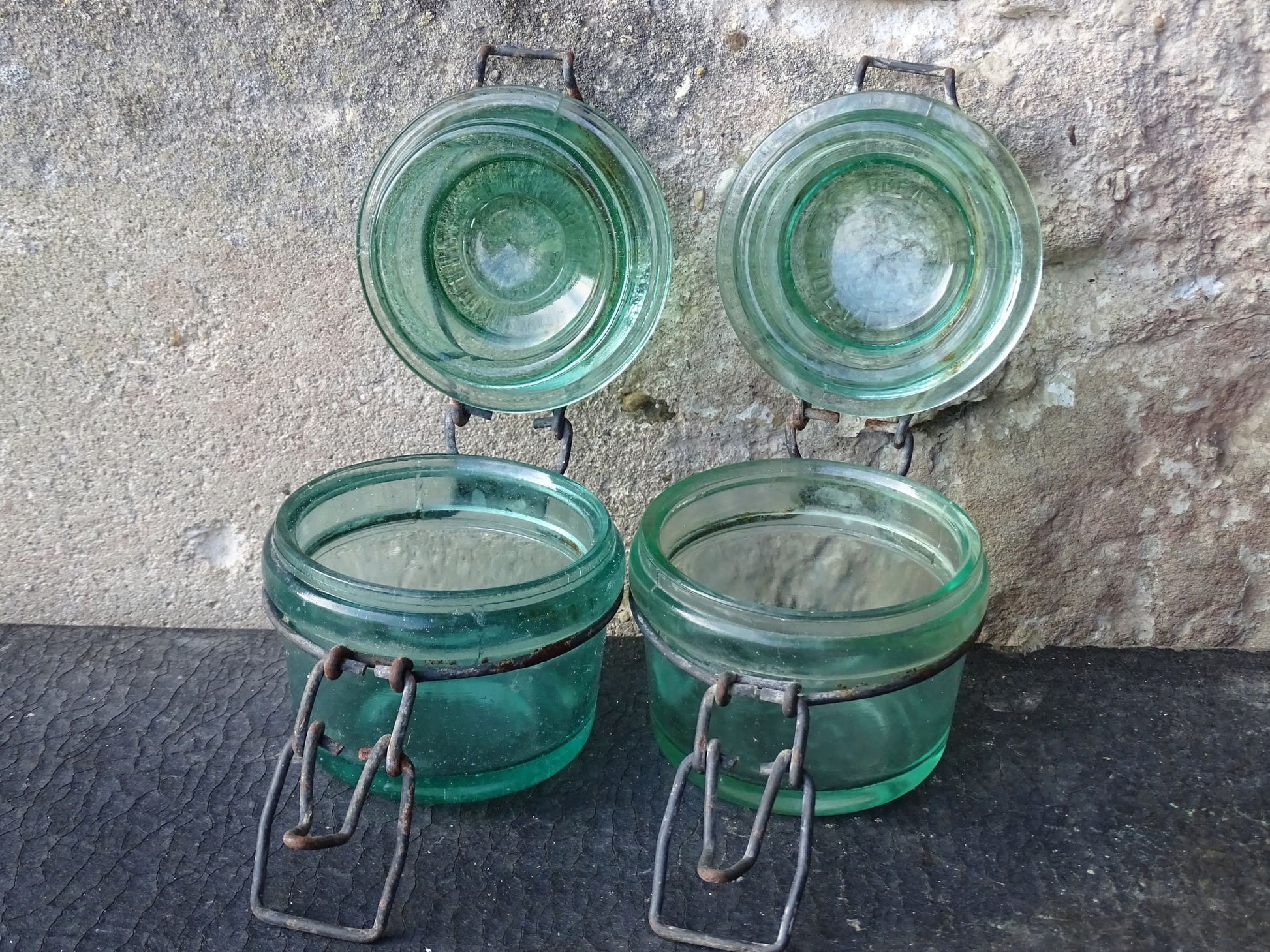 Pair of French vintage green glass preserving jars by L'Ideale. They have thick glass, embossed with the maker's name on top and original metal fasteners with a naturally aged finish. 