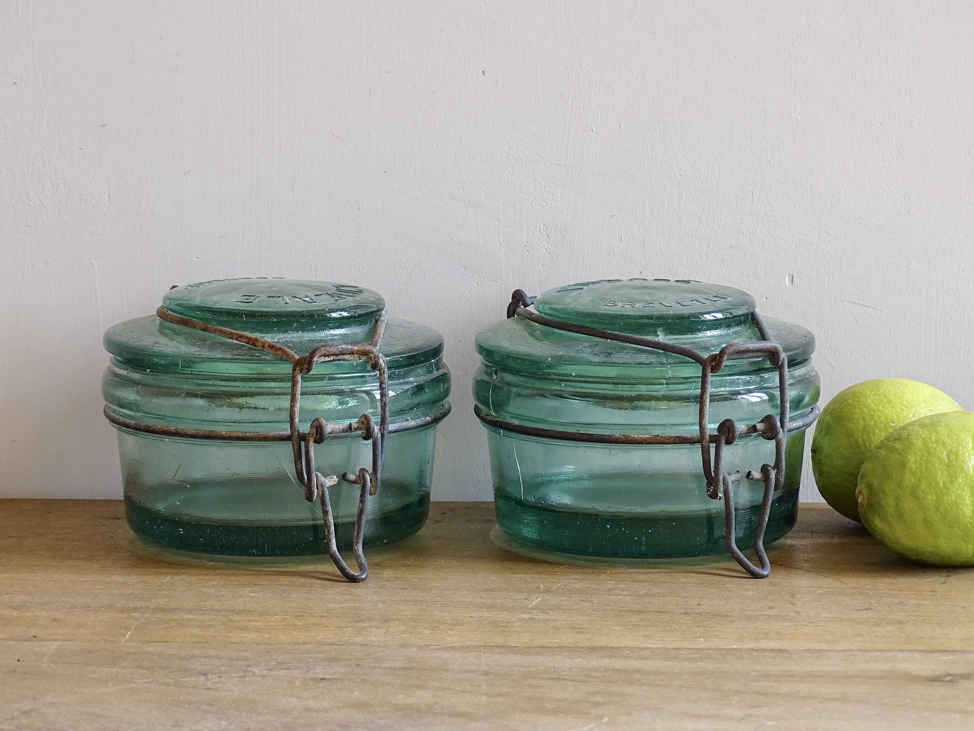 Pair of large French vintage green glass preserving jars by L'Ideale. They feature thick green glass, embossed detailing, and old metal clasps with a naturally aged finish. 