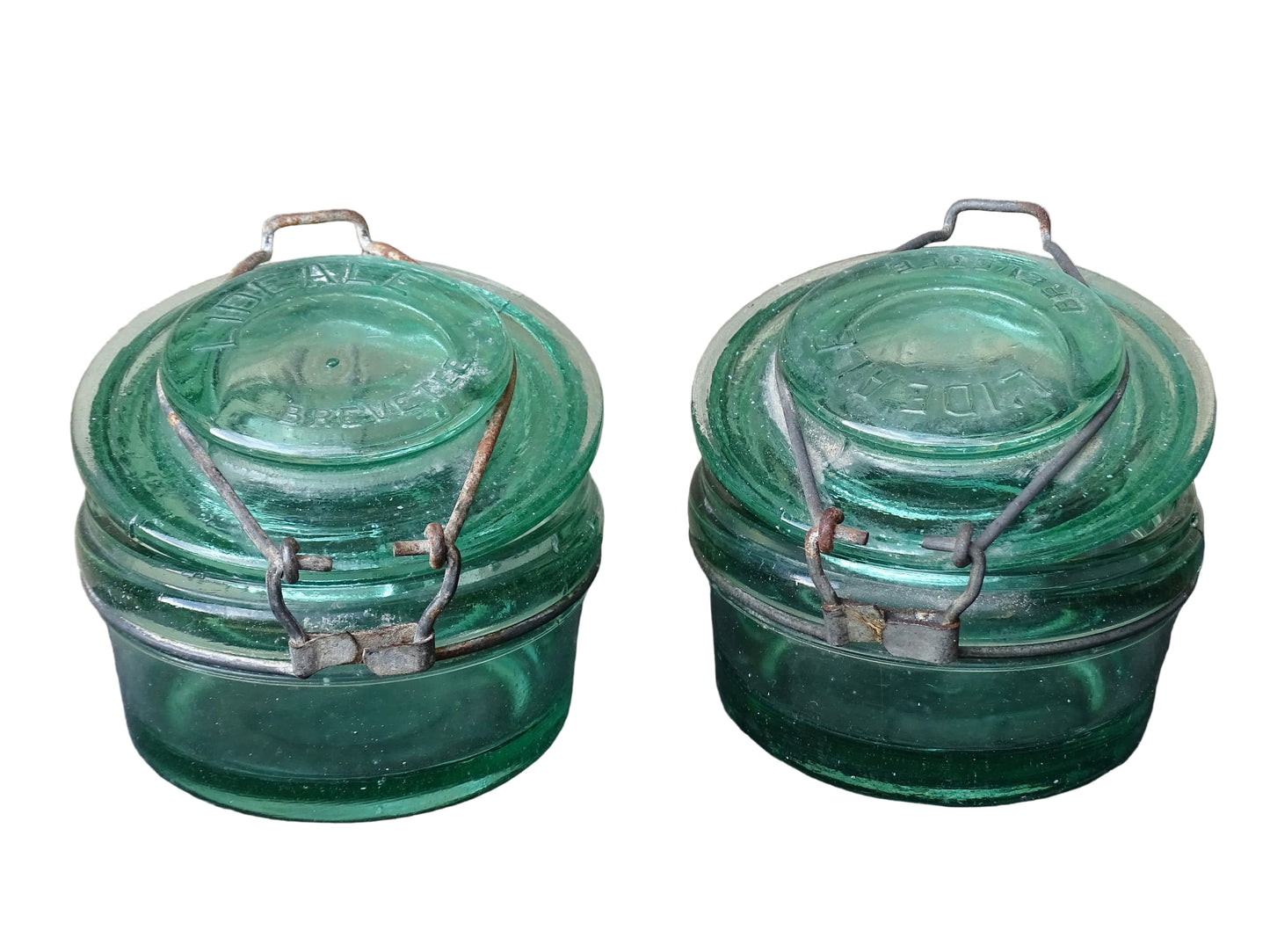 Pair of large French vintage green glass preserving jars by L'Ideale. They feature thick green glass, embossed detailing, and old metal clasps with a naturally aged finish. 