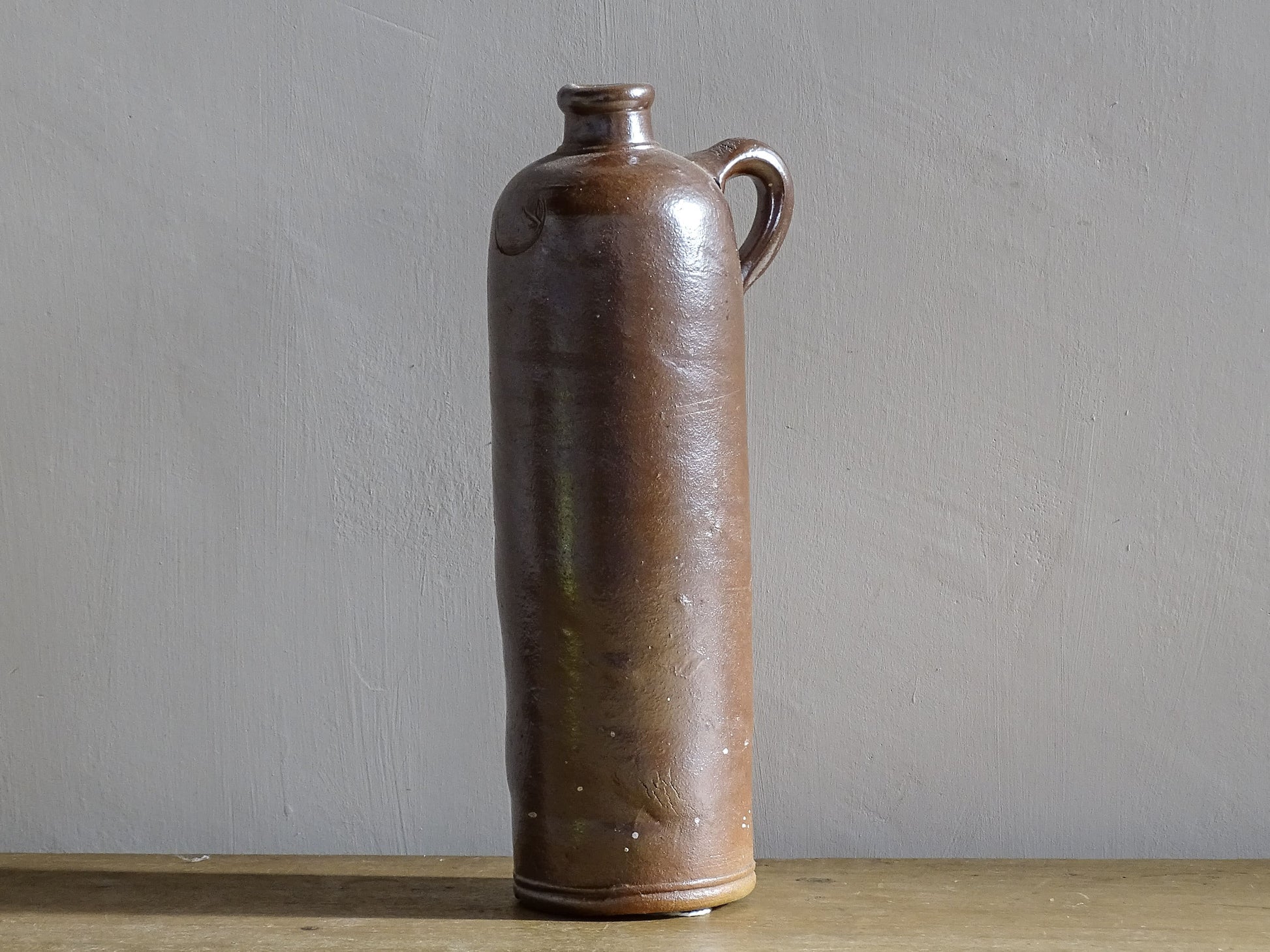 Antique salt glazed stoneware bottle, with a raised lion medallion on the shoulder and a loop handle. Bottle with textured surface and deep brown glaze. 