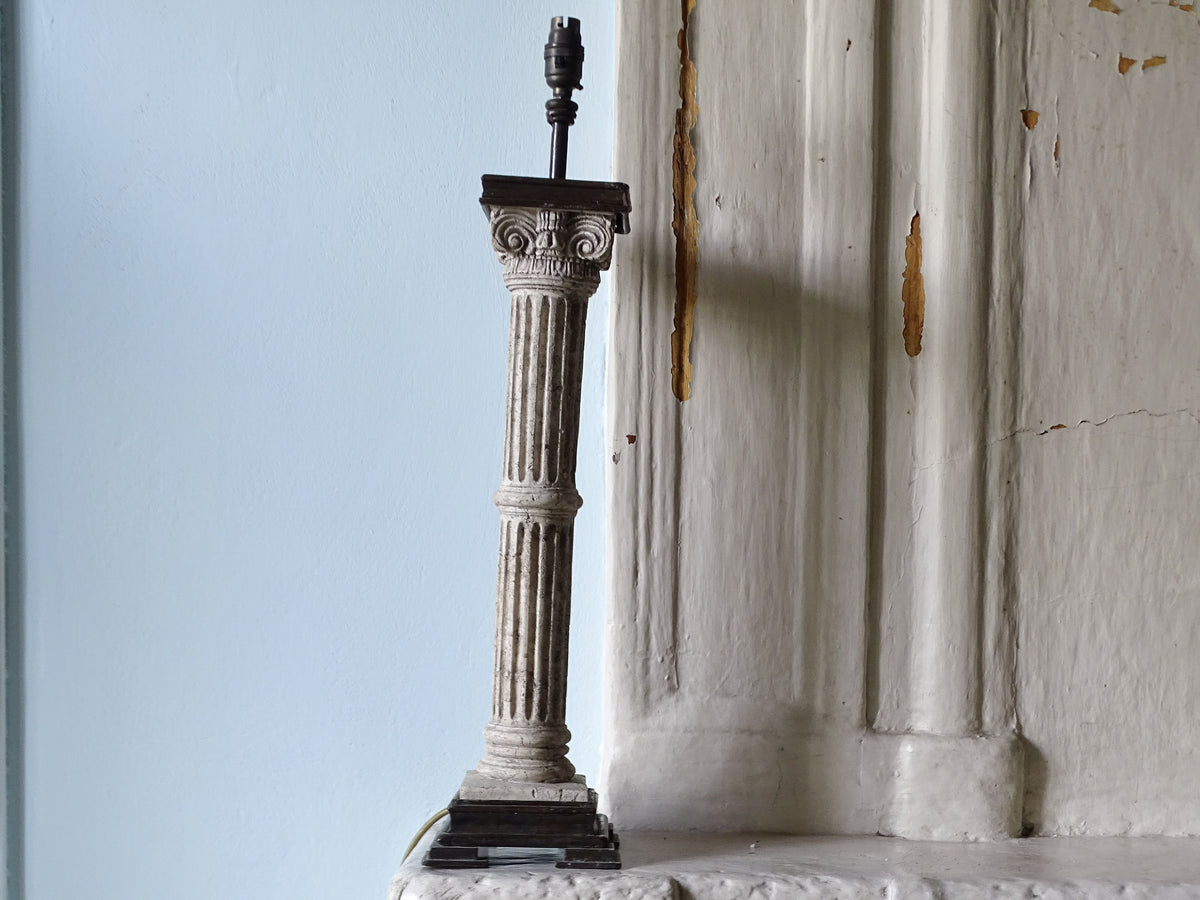 Vintage table lamp with Corinthian column base, pictured on a country house fireplace next to a pale blue wall