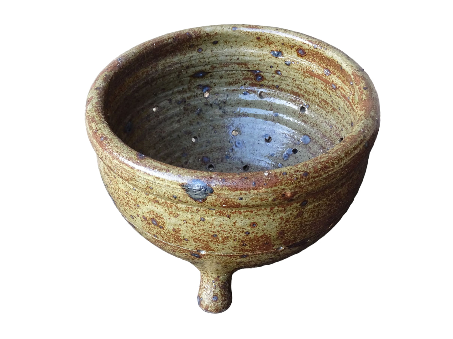 Rustic French vintage ceramic colander, stoneware berry strainer with a speckled glaze. It has a mix of warm earthy browns and olive tones, with darker fleck. It stands on three small feet and has a round form and softly curved rim.
