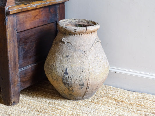 An early 19th century French antique terracotta pot, known as a ponne (salting pot), sourced in the Bordeaux region and likely Charentais in origin.
This example stands at 38 cm / 14.9" high and 32 cm / 12.6" wide. It has a particularly sculptural form, with a rounded body rising to a thick rolled rim and a simple incised band beneath the shoulder. The surface has developed a beautifully weathered patina over time, with areas of natural wear.