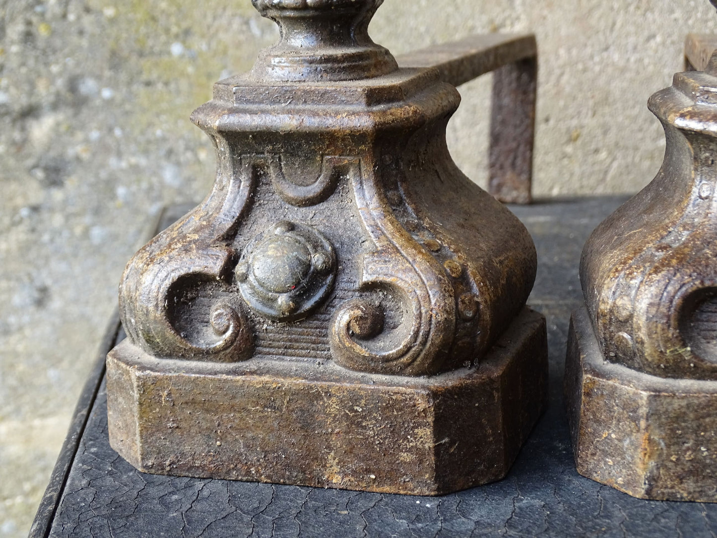 Pair of French antique cast iron andirons or fire dogs with a classical style. Each andiron is topped with an urn-shaped finial, accented by moulded details and a fluted form that evokes neoclassical architectural design. The bases are decorated with scrolling motifs and small medallions. 