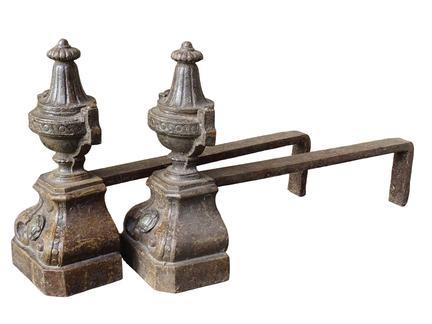 Pair of French antique cast iron andirons or fire dogs with a classical style. Each andiron is topped with an urn-shaped finial, accented by moulded details and a fluted form that evokes neoclassical architectural design. The bases are decorated with scrolling motifs and small medallions. 