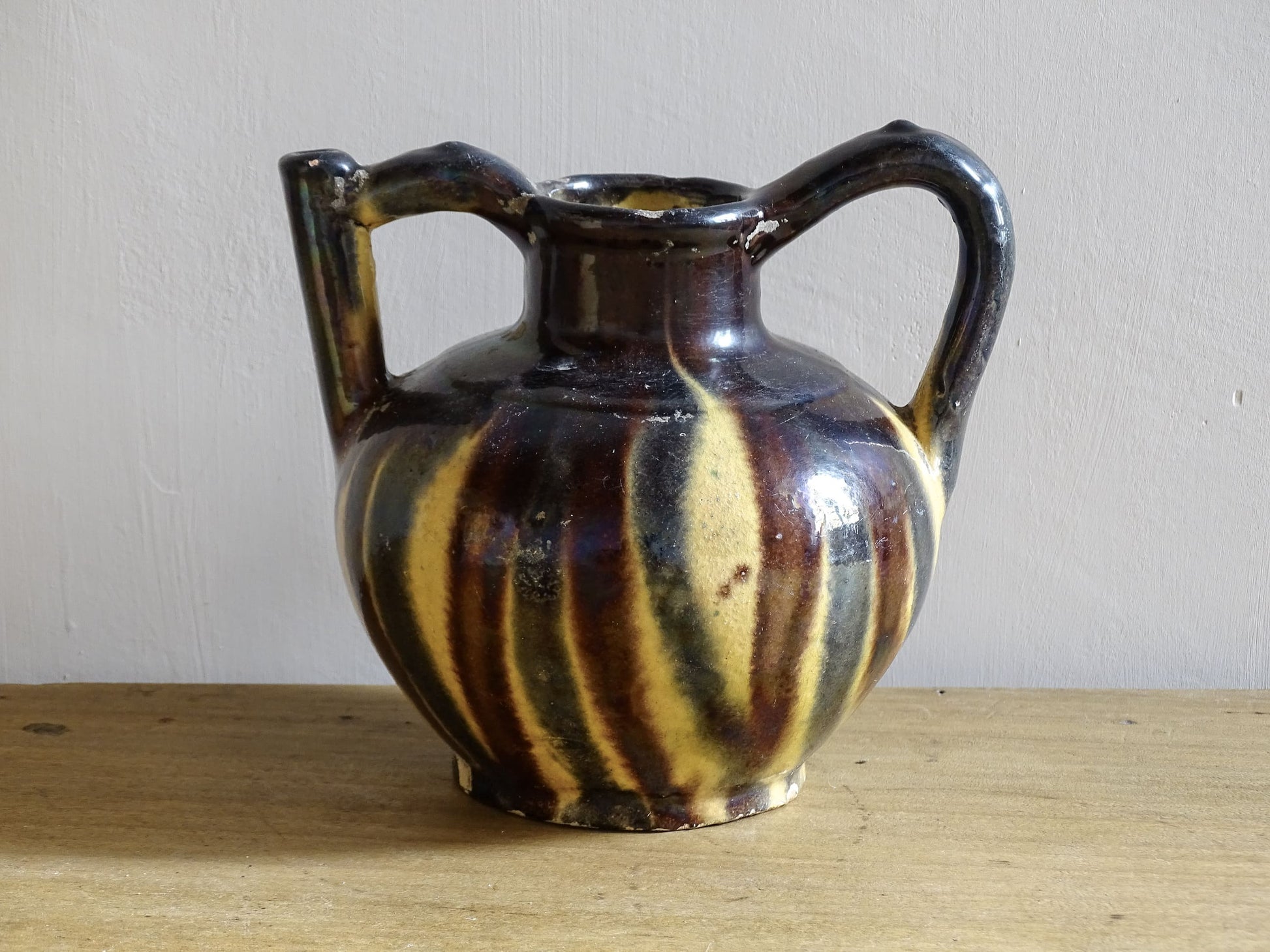 French antique ceramic jug or orjol with striped glaze. Glazed terracotta pitcher with yellow, black and brown glaze. 