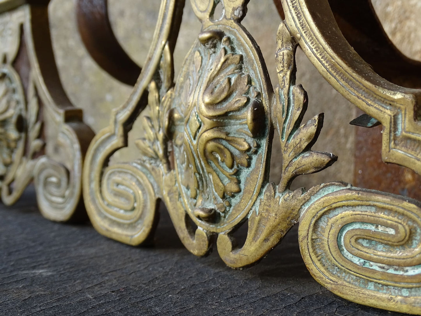 Pair of French antique brass andirons or fire dogs in a Louis XVI revival style. Each andiron is topped with a turned baluster finial. The pierced front plates display an ornate composition of acanthus leaves, scrollwork, and a central oval cartouche framed by laurel branches, typical of neoclassical design.