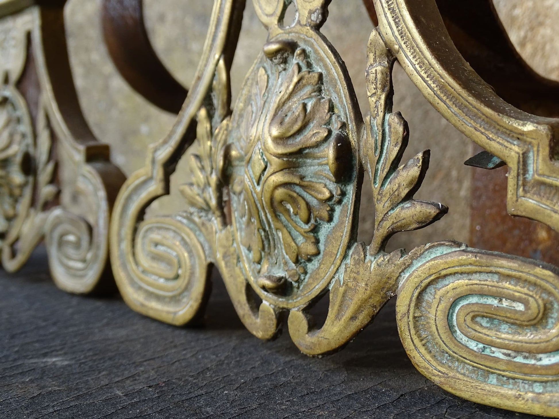 Pair of French antique brass andirons or fire dogs in a Louis XVI revival style. Each andiron is topped with a turned baluster finial. The pierced front plates display an ornate composition of acanthus leaves, scrollwork, and a central oval cartouche framed by laurel branches, typical of neoclassical design.