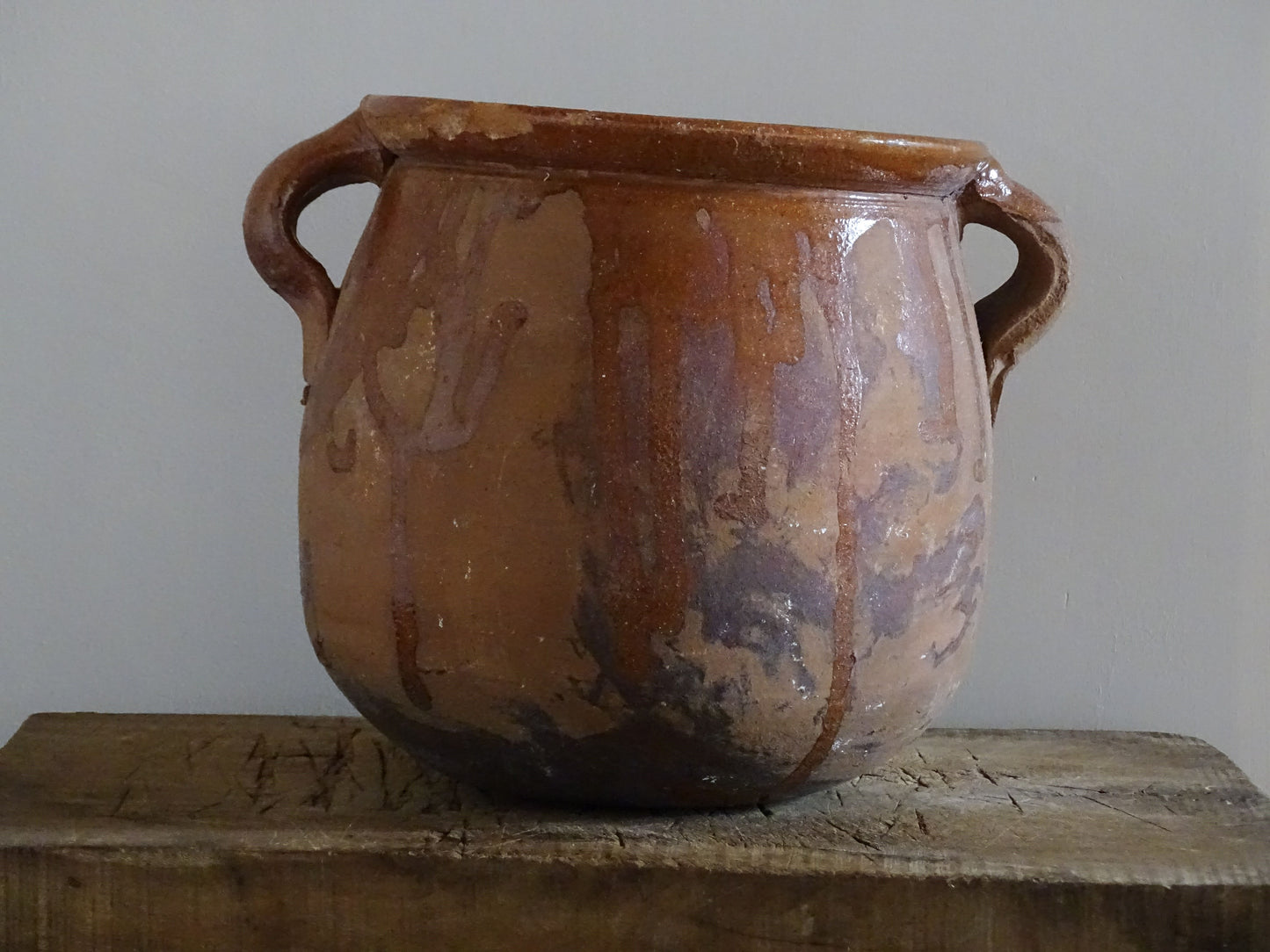 French vintage terracotta pot with orange glaze interior and drip glaze around the sides. Earthenware confit jar with two handles and a curved base.