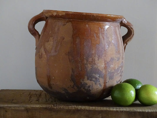 French vintage terracotta pot with orange glaze interior and drip glaze around the sides. Earthenware confit jar with two handles and a curved base.