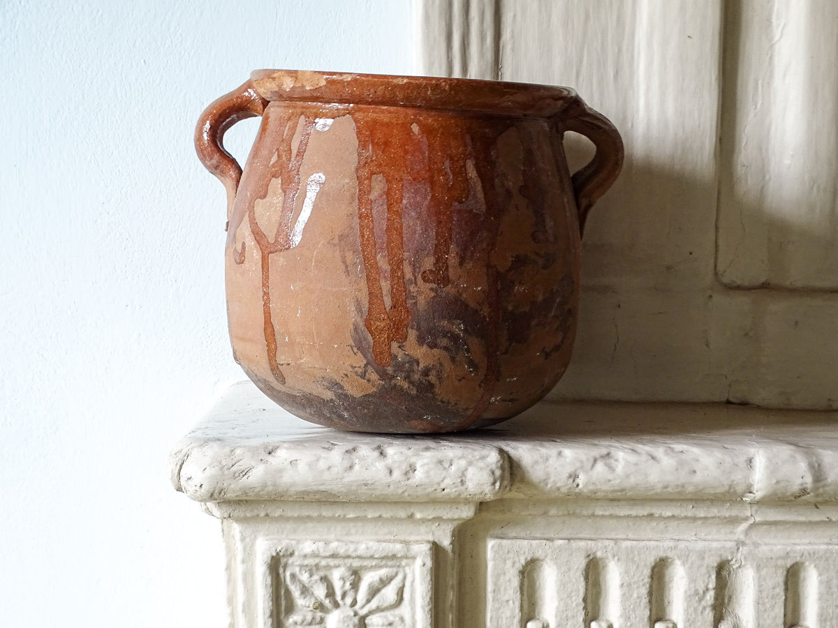 French antique terracotta pot with an orange glaze on an old country house fireplace mantel