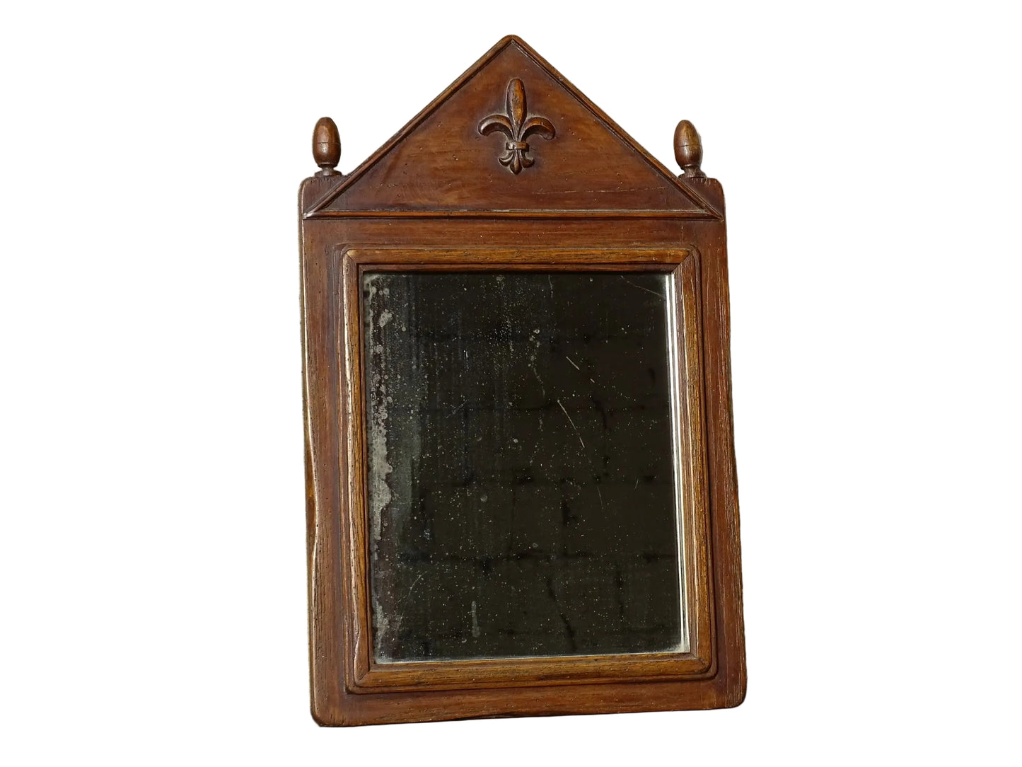 French antique wooden mirror with fleur de lis motif. The wood mirror is topped by a pediment with two turned finials.