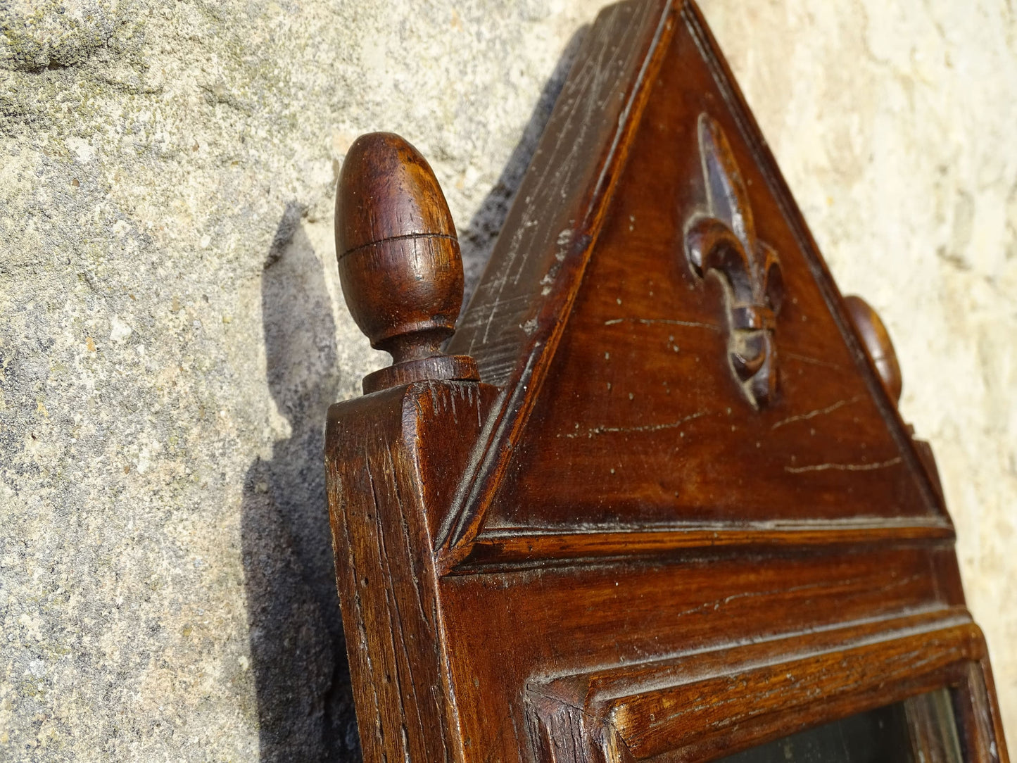 French antique wooden mirror with fleur de lis motif. The wood mirror is topped by a pediment with two turned finials.