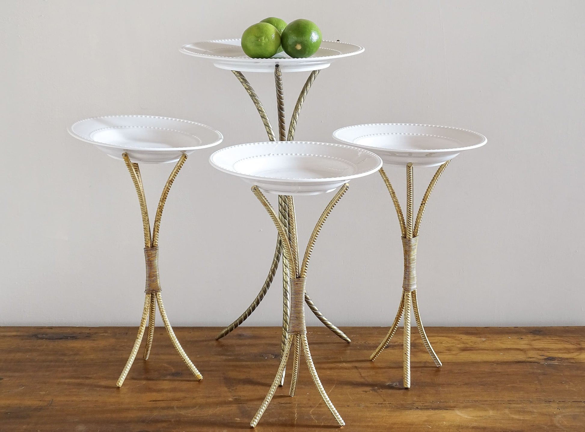 This is a collection of four French vintage plate stands dates to the 1980s. Their simple, elegant shape would suit many interior design aesthetics. They are made from gilt metal and are a tripod design.