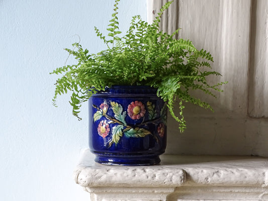 French antique ceramic planter with blue glaze and pink flowers filled with a green fern, pictured on a country house fireplace.