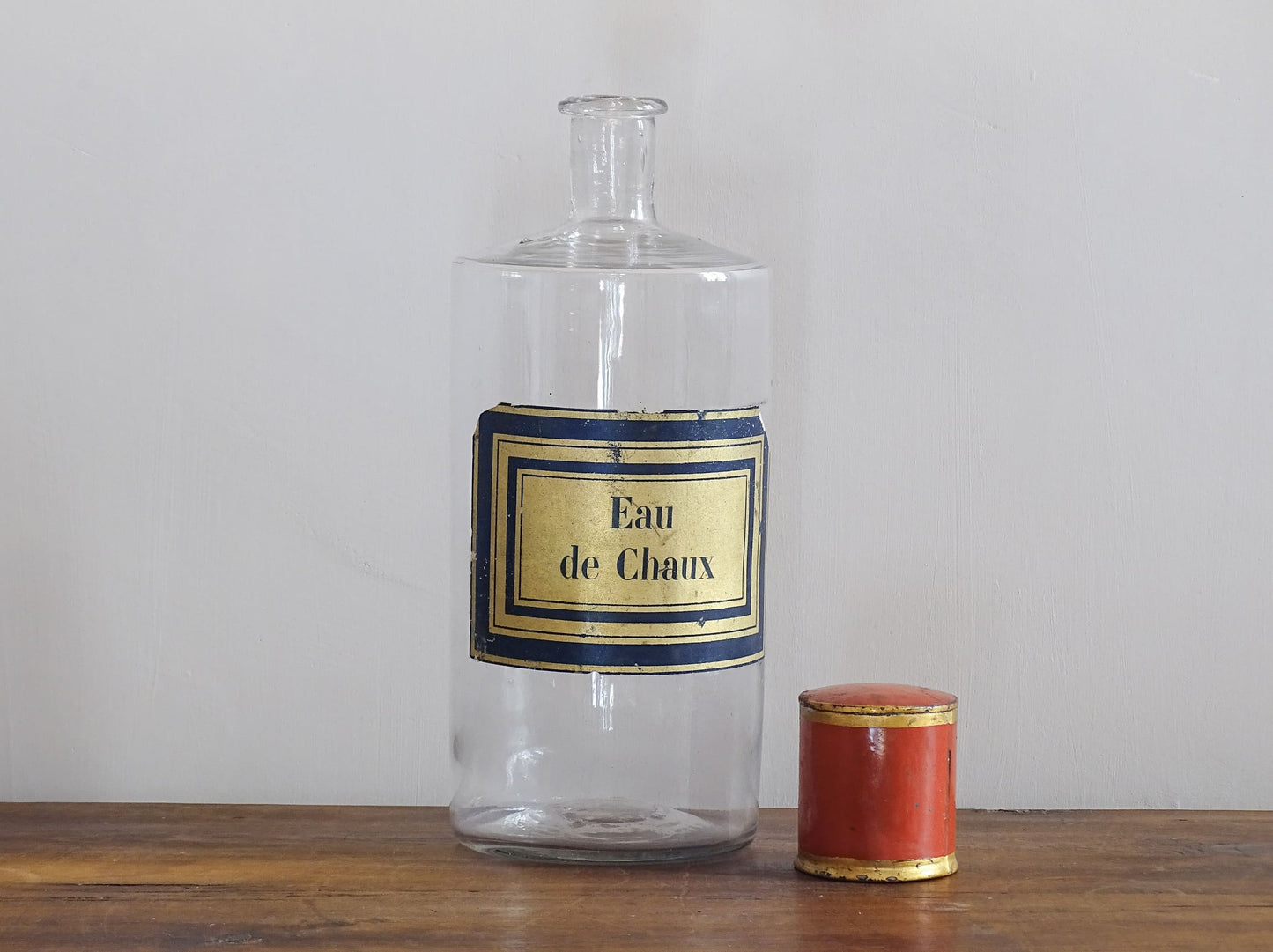 A French antique glass apothecary bottle with original, red and gold, painted metal top and original paper label. The label reads: Eau de Chaux (Lime Water). This antique glass bottle is hand blown and dates to the late 1800's. 
