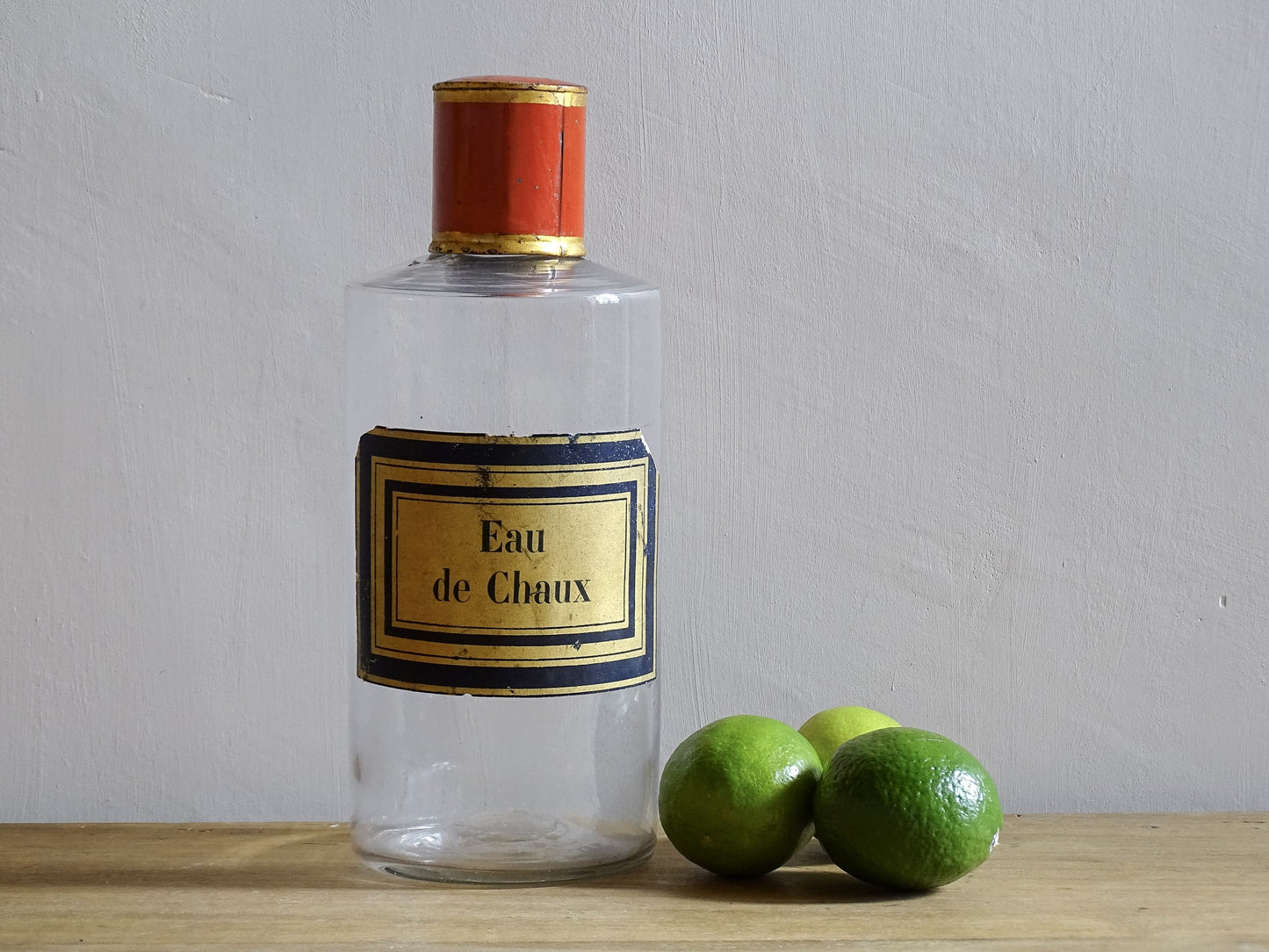 A French antique glass apothecary bottle with original, red and gold, painted metal top and original paper label. The label reads: Eau de Chaux (Lime Water). This antique glass bottle is hand blown and dates to the late 1800's. 