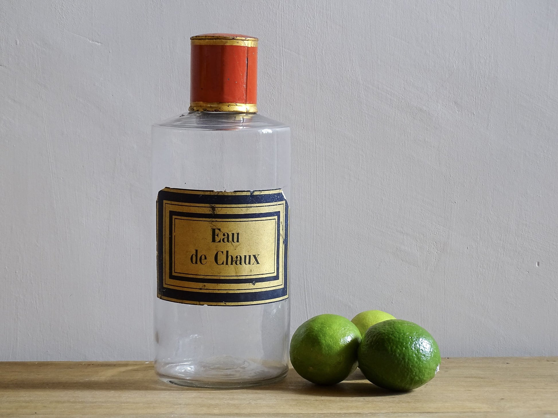 A French antique glass apothecary bottle with original, red and gold, painted metal top and original paper label. The label reads: Eau de Chaux (Lime Water). This antique glass bottle is hand blown and dates to the late 1800's. 