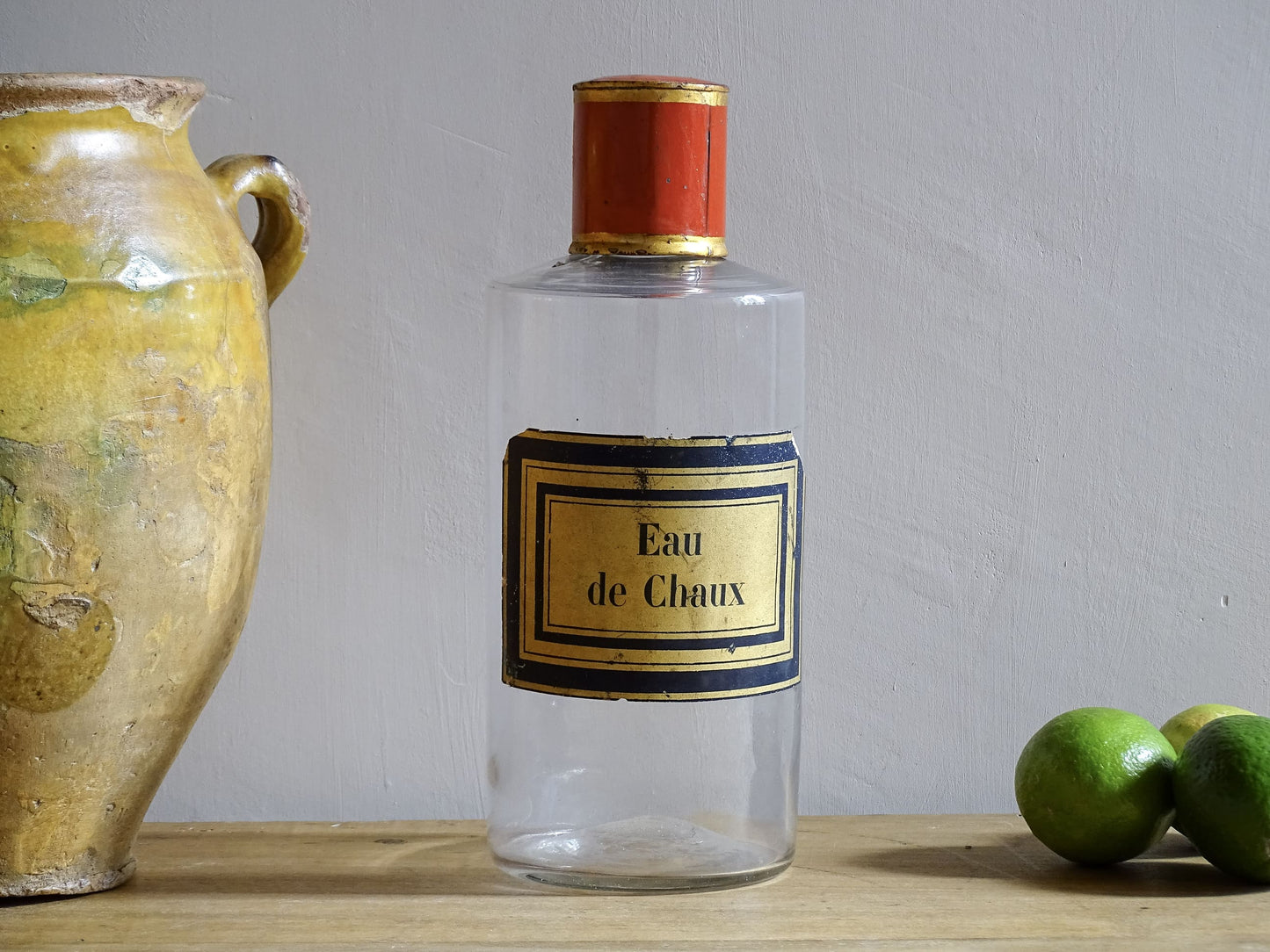 A French antique glass apothecary bottle with original, red and gold, painted metal top and original paper label. The label reads: Eau de Chaux (Lime Water). This antique glass bottle is hand blown and dates to the late 1800's. 
