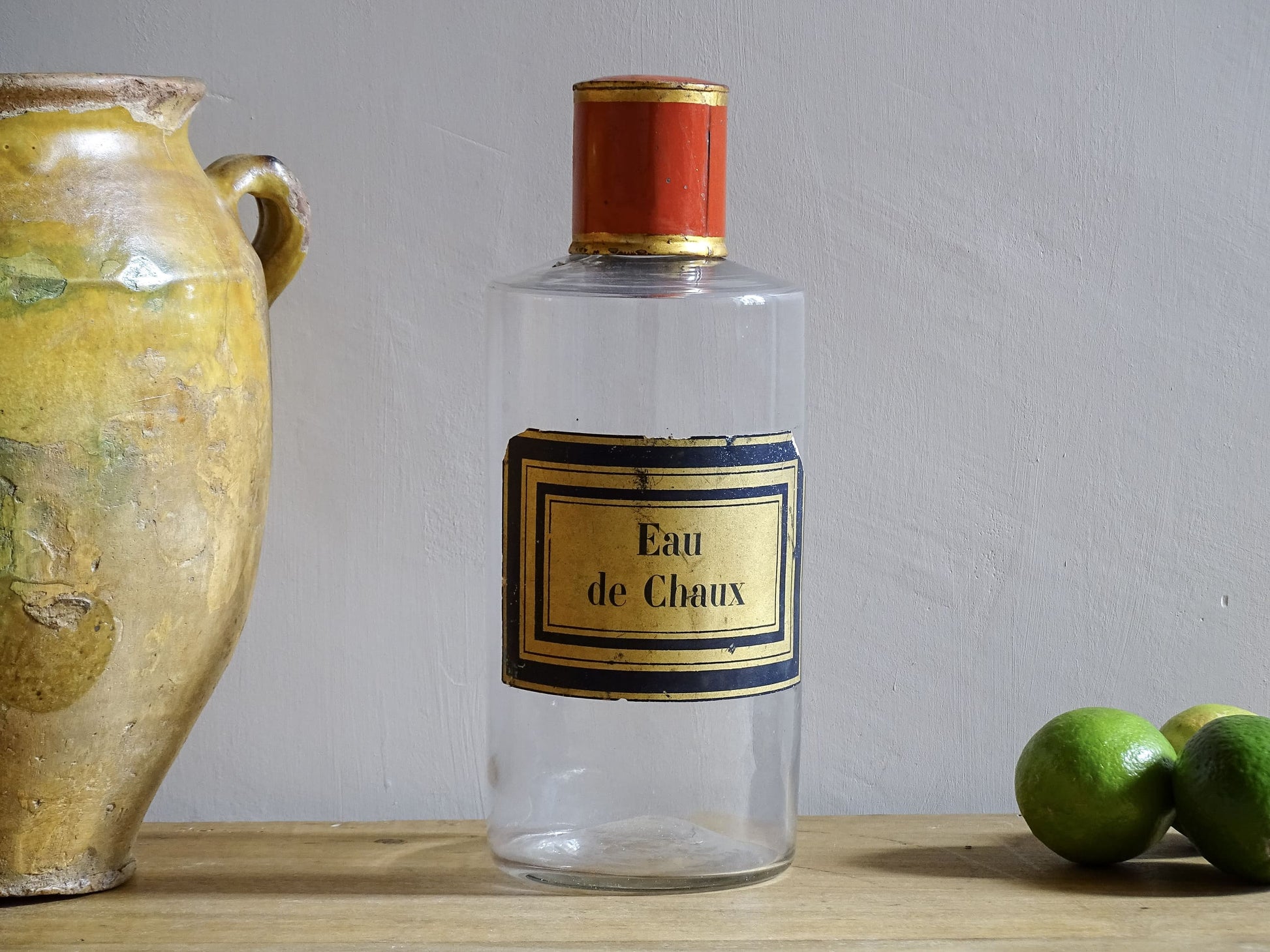 A French antique glass apothecary bottle with original, red and gold, painted metal top and original paper label. The label reads: Eau de Chaux (Lime Water). This antique glass bottle is hand blown and dates to the late 1800's. 