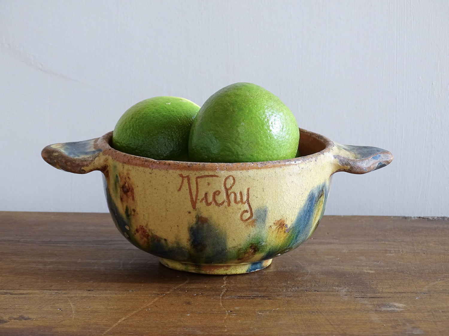 A French vintage ceramic souvenir bowl from Vichy, in the Auvergne region of France. Decorated with hand-applied sponged slip in yellow, green and blue tones. Mid 20th century, with a warm rustic glaze and visible age-related crazing.