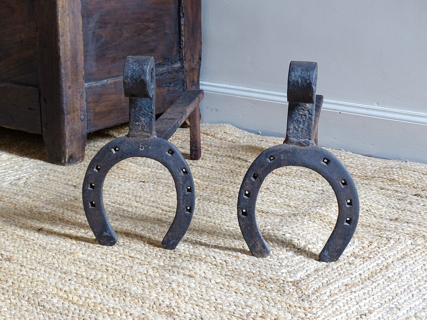  pair of French antique wrought iron andirons or fire dogs, date to the 19th century. They incorporate hand-forged horseshoes, with square-punched nail holes and substantial rear supports. A rustic, agricultural design with authentic forge marks throughout.