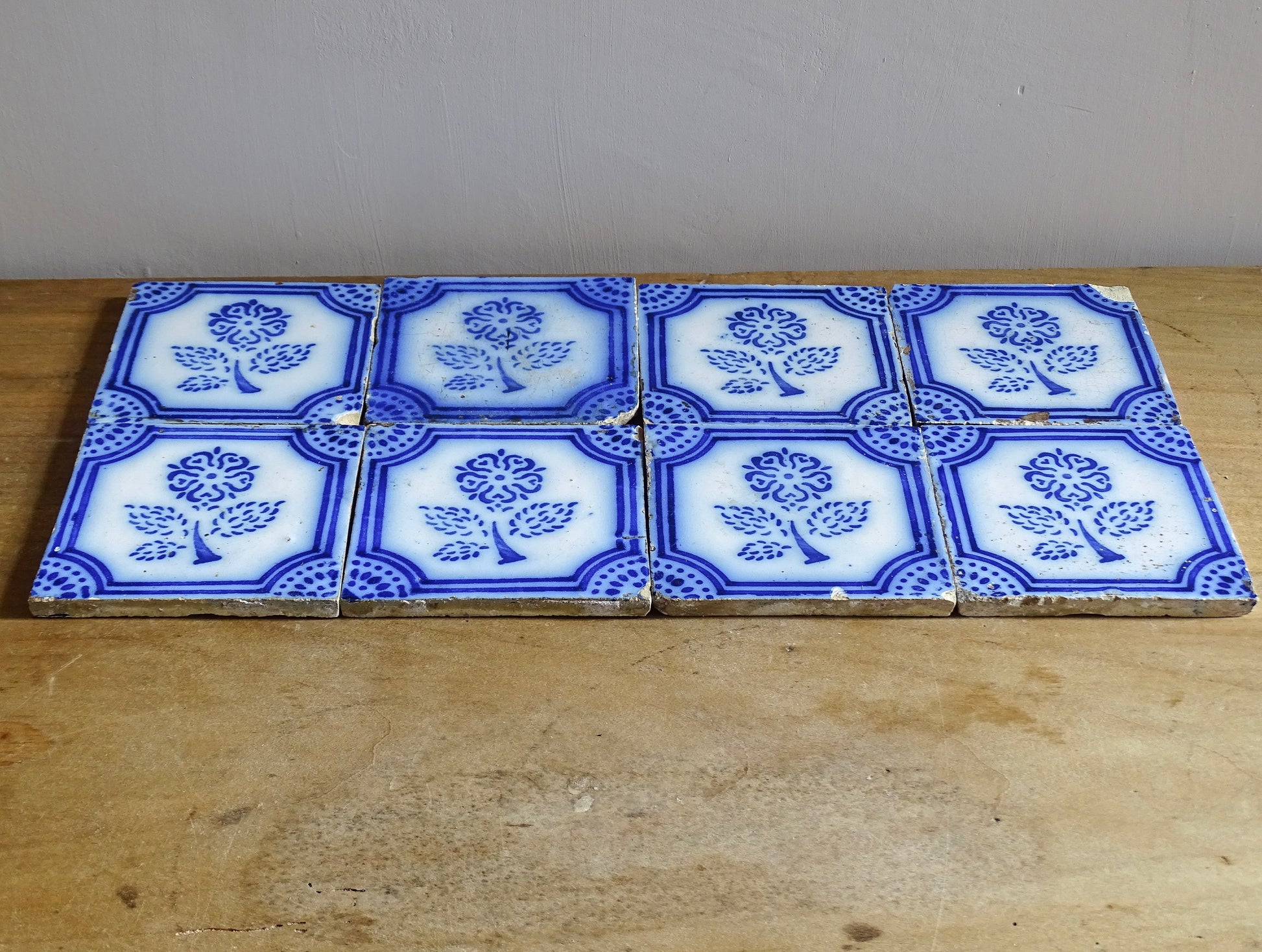 A set of eight French antique Desvres faience tiles in blue &amp; white. These transfer printed, earthenware tiles were manufactured in the late 1900's in Desvres, Northern France. Six of the tiles are back-stamped. They are beautifully transfer printed in cobalt blue. A floral sprig sits in the centre of the cartouche framing.