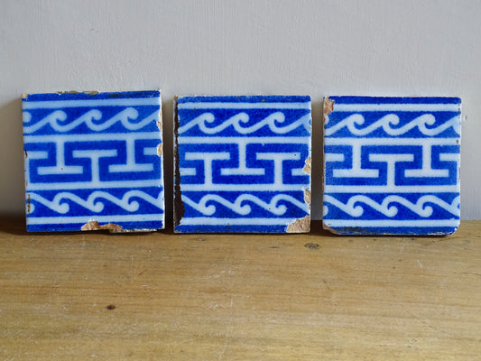 A set of three French antique Desvres faience tiles in blue &amp; white. These transfer printed, earthenware tiles were manufactured in the late 1900's in Desvres, Northern France. These antique tiles are back-stamped with the maker's mark. They are beautifully transfer printed in cobalt blue with a repeating Greek key motif and stylised wave border.