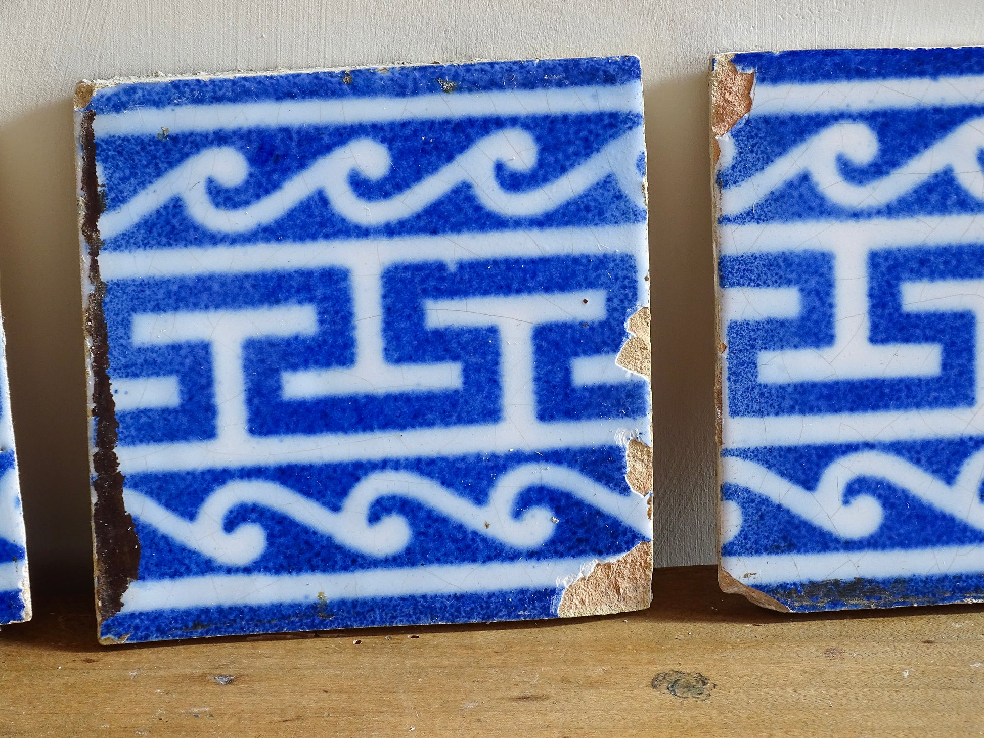 A set of three French antique Desvres faience tiles in blue &amp; white. These transfer printed, earthenware tiles were manufactured in the late 1900's in Desvres, Northern France. These antique tiles are back-stamped with the maker's mark. They are beautifully transfer printed in cobalt blue with a repeating Greek key motif and stylised wave border.
