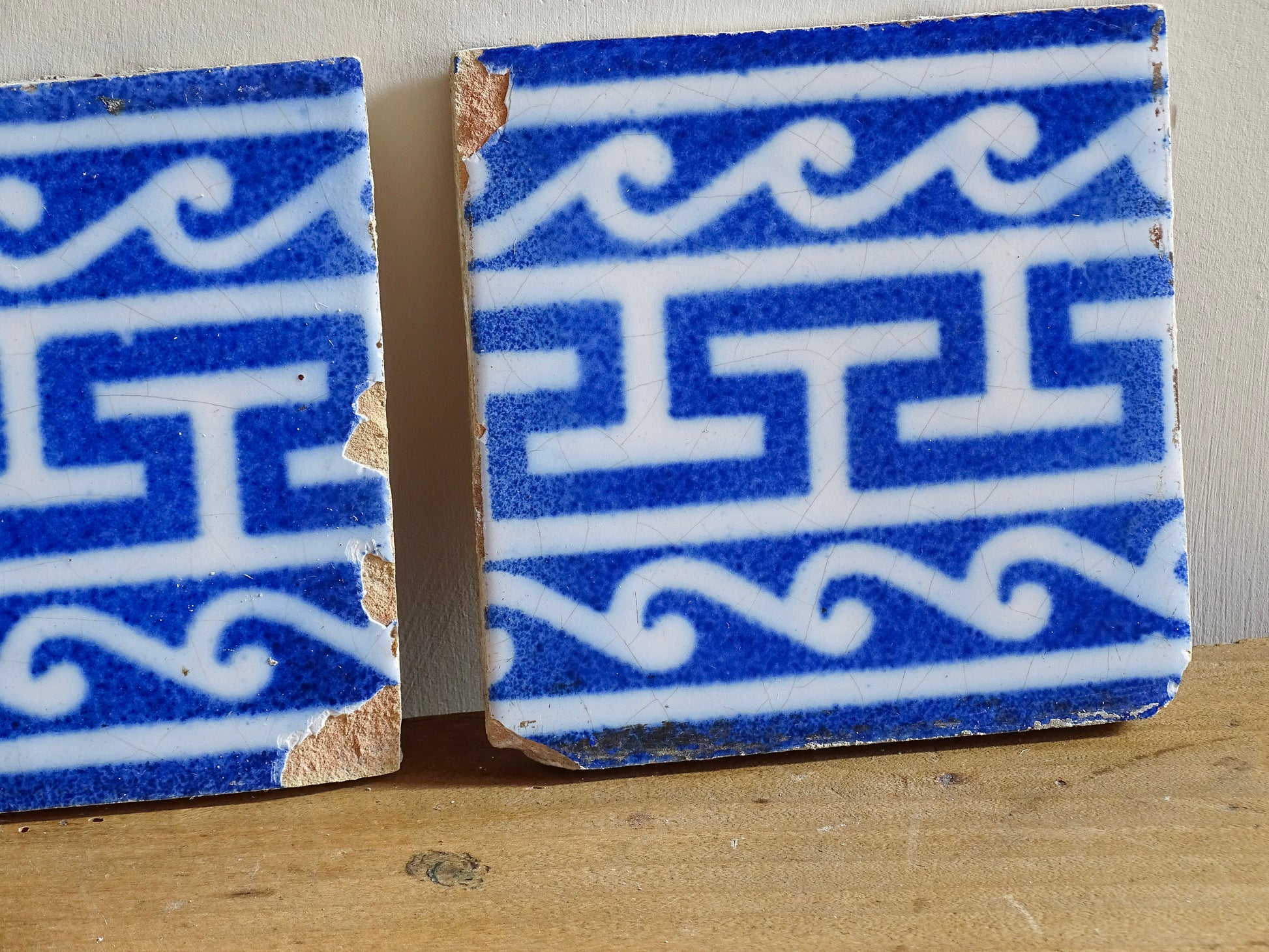 A set of three French antique Desvres faience tiles in blue &amp; white. These transfer printed, earthenware tiles were manufactured in the late 1900's in Desvres, Northern France. These antique tiles are back-stamped with the maker's mark. They are beautifully transfer printed in cobalt blue with a repeating Greek key motif and stylised wave border.