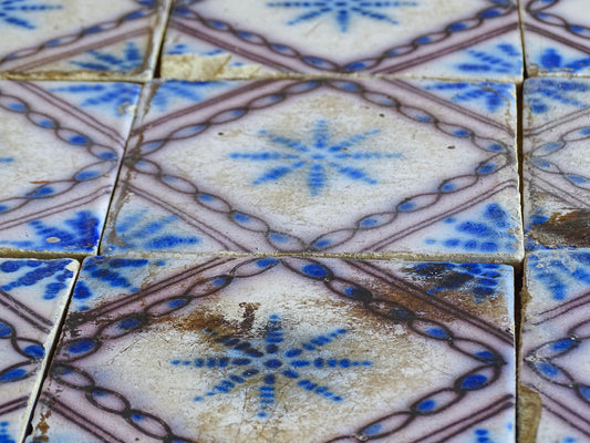 A set of nine French antique Desvres faience tiles in blue &amp; white. These transfer printed, earthenware tiles were manufactured in the late 1900's in Desvres, Northern France. The tiles are back-stamped. Each tile is decorated in cobalt blue on a white tin-glazed ground, centred with a stylised starburst motif and framed within a manganese-purple diamond border.