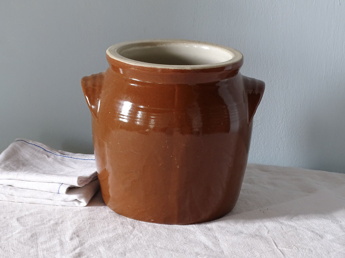 French vintage ceramic jar with brown glaze, pictured with antique linen in front of a pale blue wall