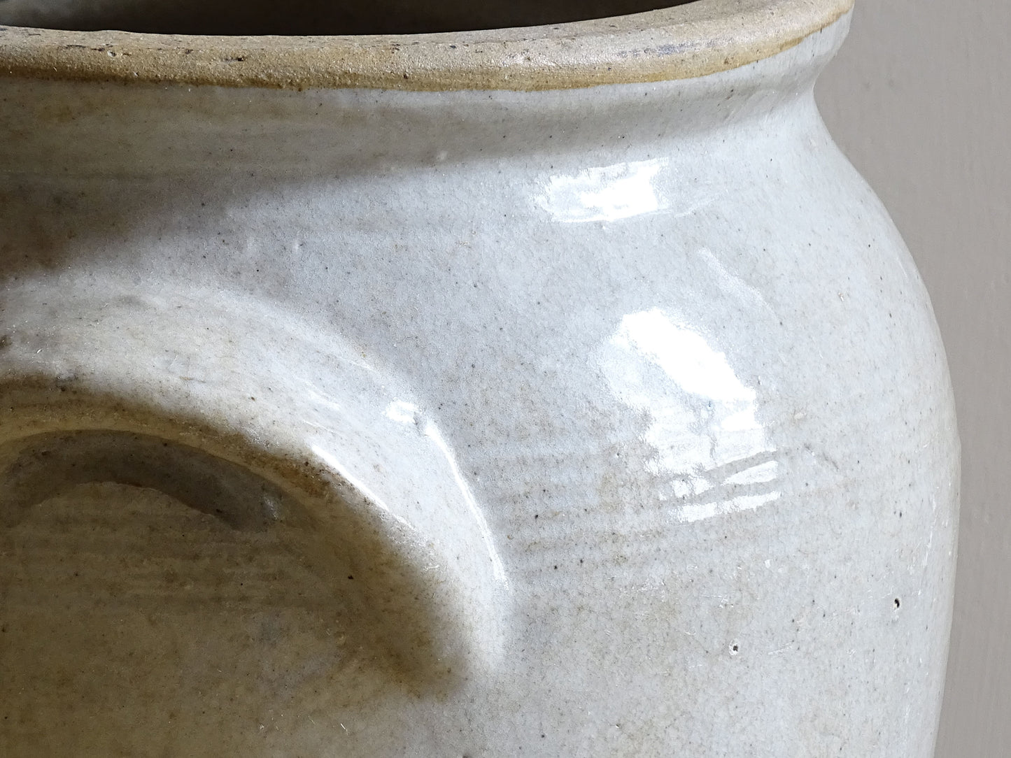 Close up of an antique stoneware jar or French confit pot with a beige glaze and two handles in a rustic country kitchen style.
