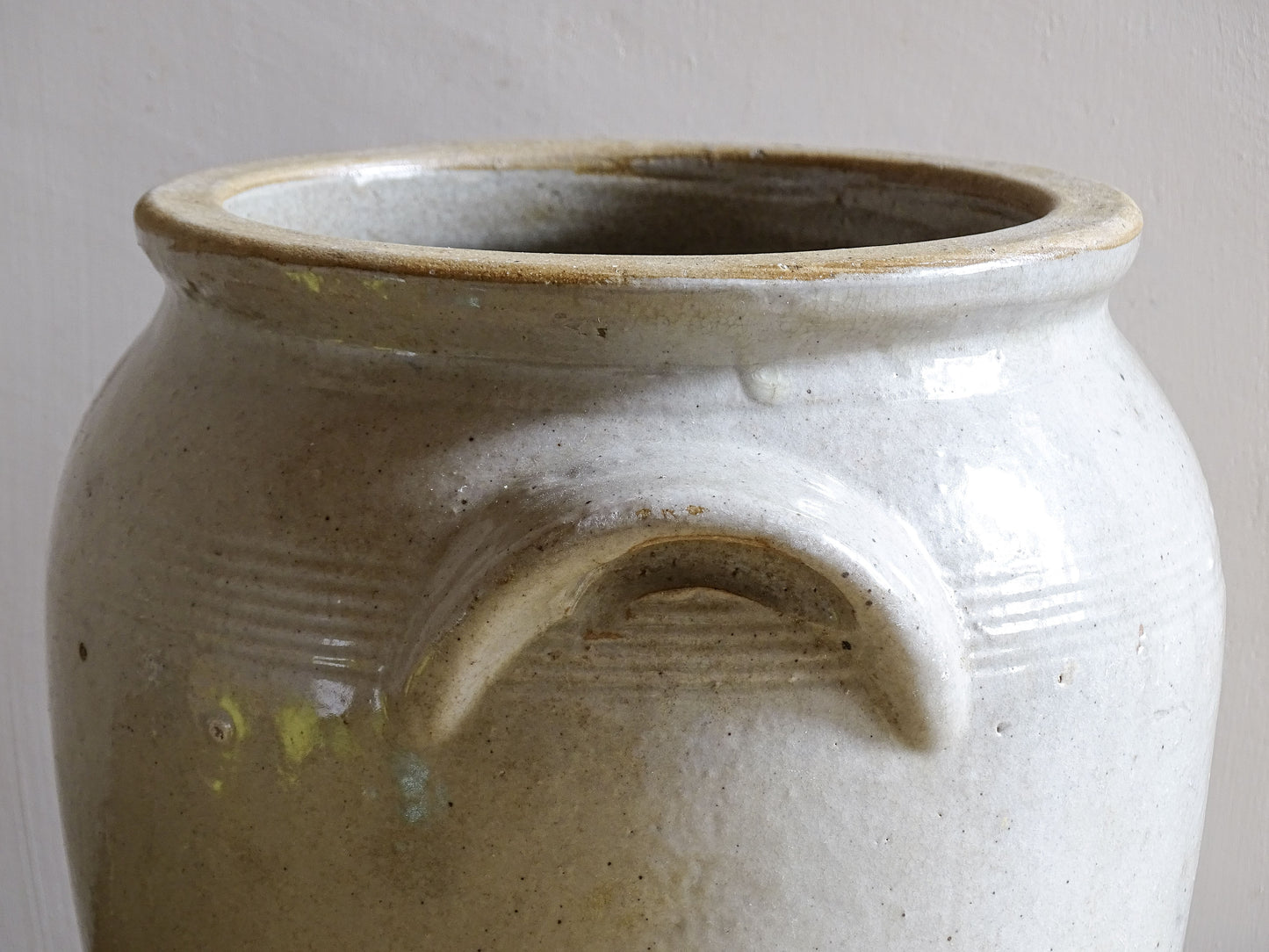 Close up of the handle of an antique stoneware jar or French confit pot with a beige glaze and two handles in a rustic country kitchen style.