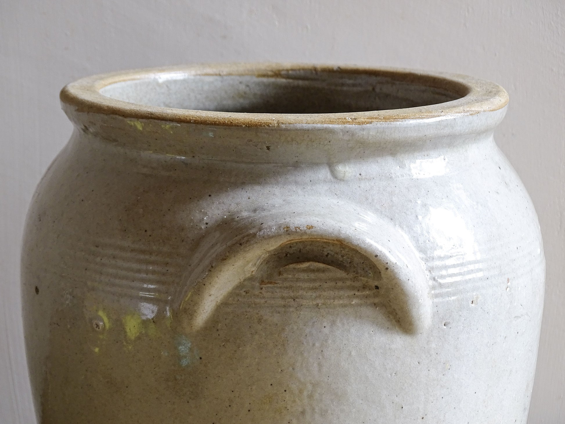 Close up of the handle of an antique stoneware jar or French confit pot with a beige glaze and two handles in a rustic country kitchen style.
