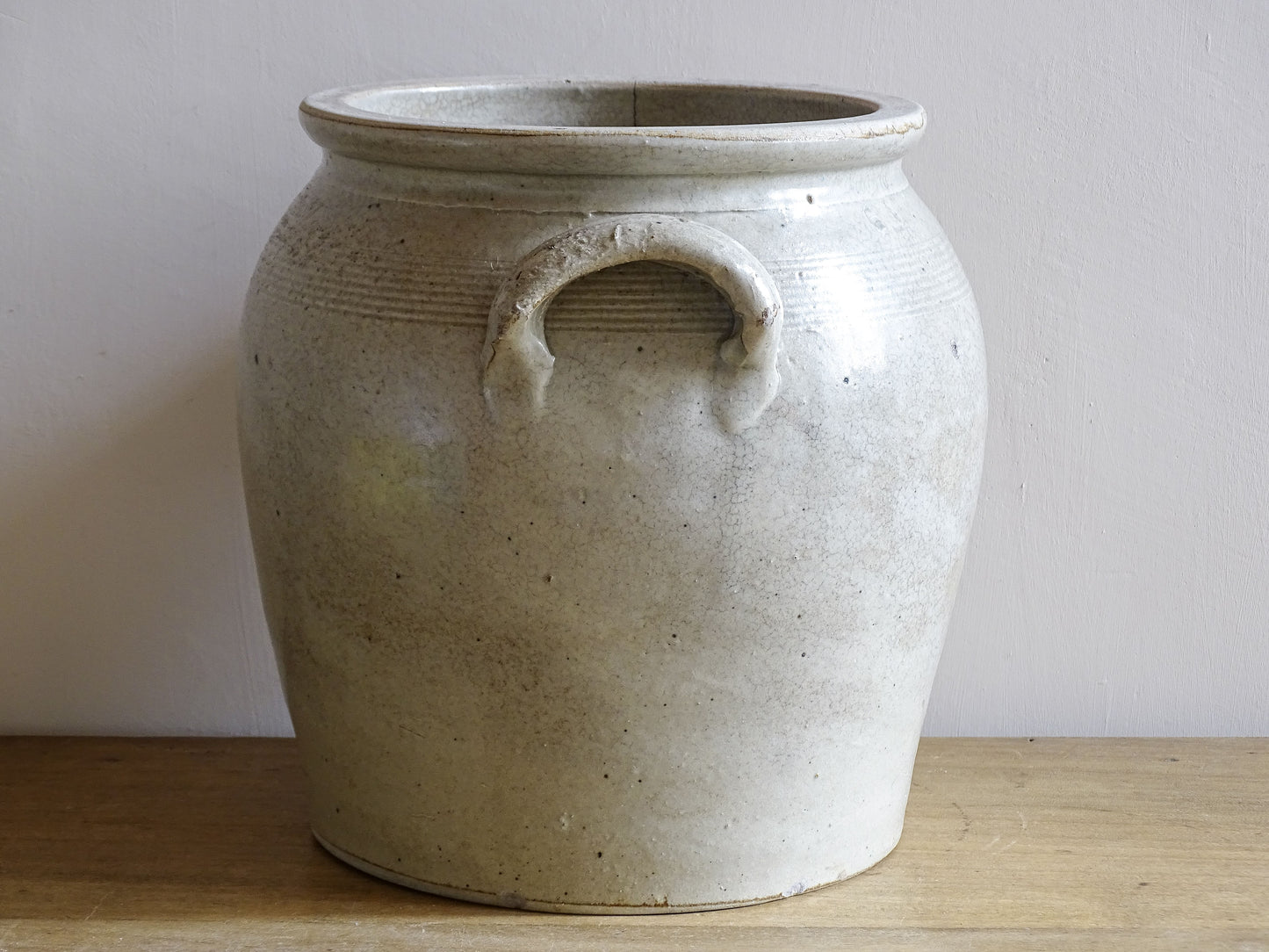 Side view of a French antique stoneware confit jar with a pale beige glaze
