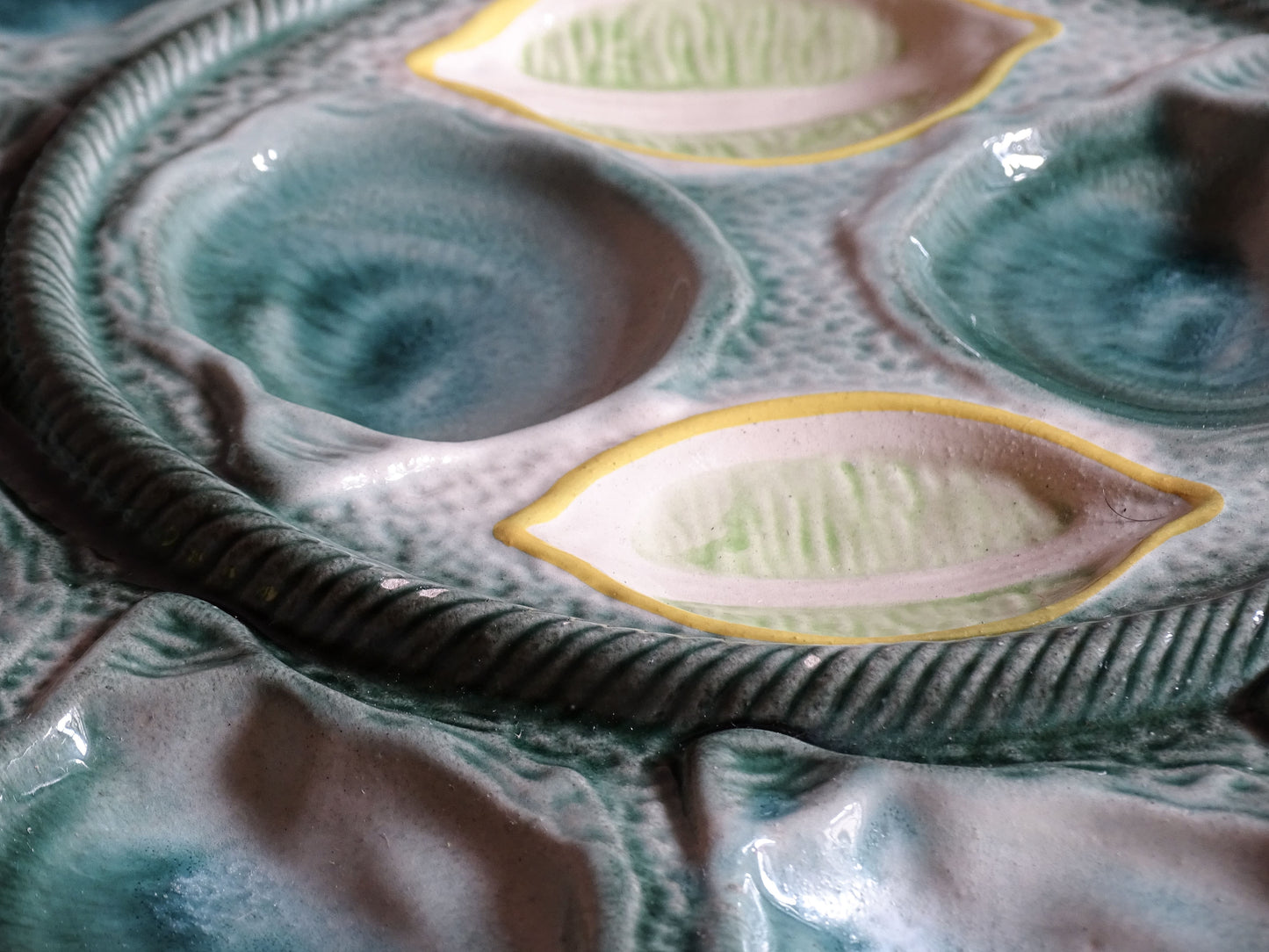 Close view of shell-shaped wells on a green glazed vintage French oyster serving plate by St Clément.