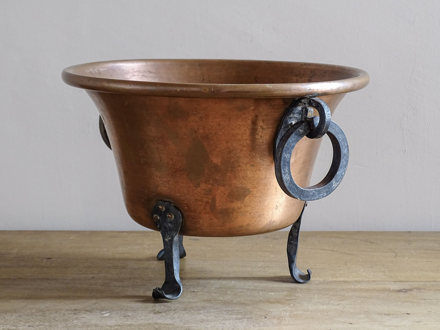 Side view of vintage copper planter with iron ring handles and curved wrought iron feet.
